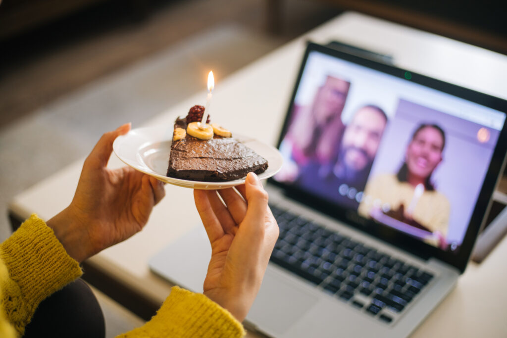 Woman holding slice of birthday cake up to camera on video call.